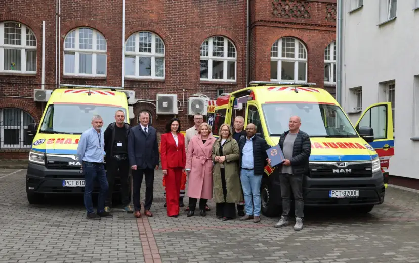 Grupa osób pozuje przed dwoma ambulansami. Jeden z mężczyzn trzyma dokument, być może związany z czn rejestracja.