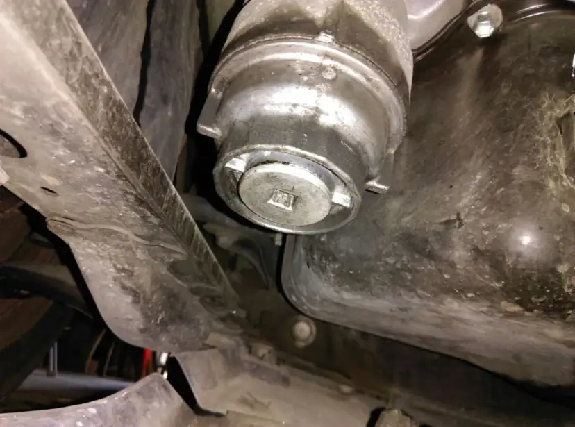 Filtre à huile de voiture sous le véhicule, avec une clé carrée insérée.