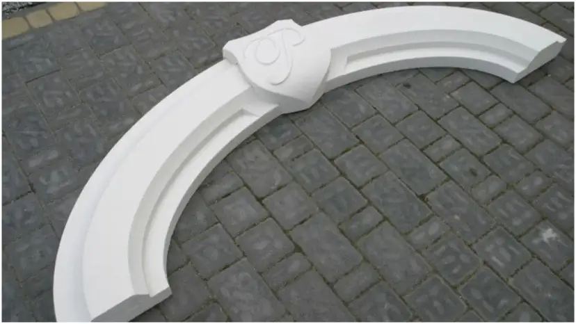Biały, ozdobny łuk nad drzwiami z herbem, gotowy do montażu. Idealny, by nadać wejściu elegancki charakter.