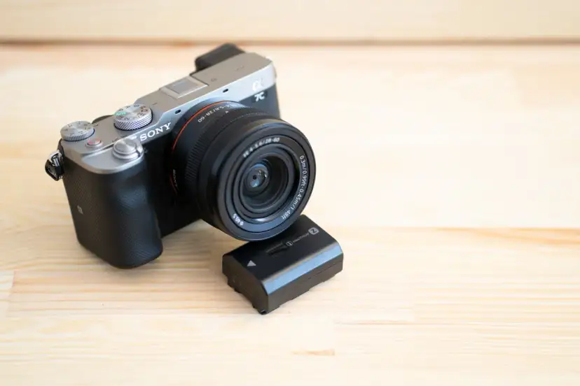 Srebrno-czarny aparat Sony a7c z obiektywem i zapasową baterią na drewnianym tle.