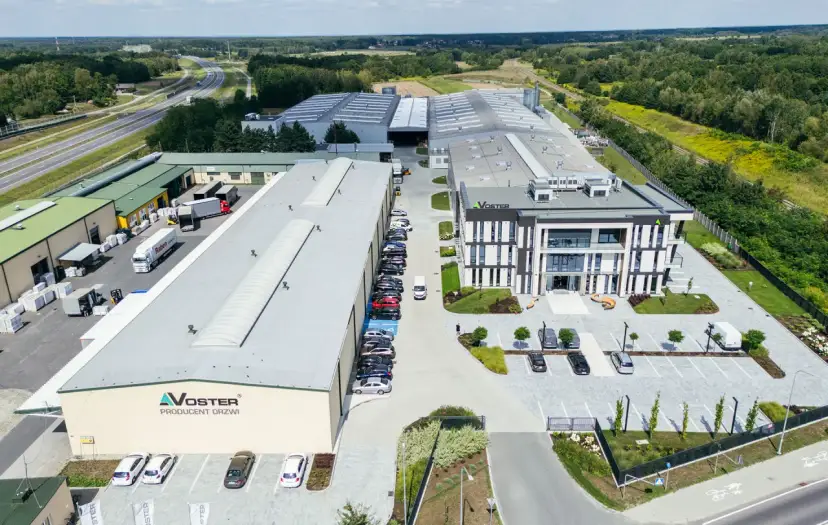 Nowoczesny kompleks produkcyjny Voster producent drzwi, z drogą szybkiego ruchu w tle.