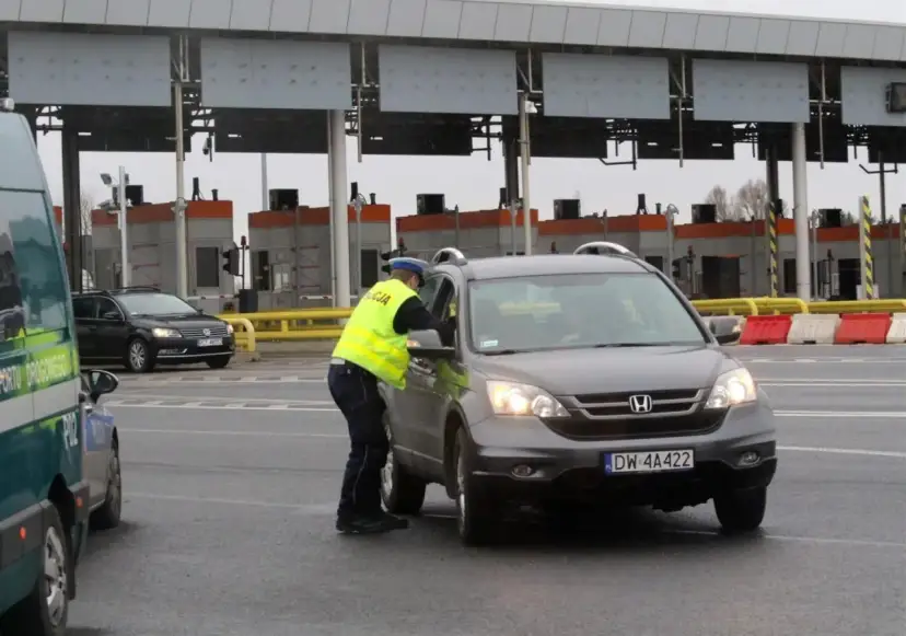 Policjant w kamizelce odblaskowej rozmawia z kierowcą przy bramkach. Czy autostrada A4 jest płatna? Tak, w tym miejscu pobierane są opłaty.
