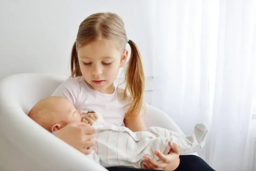 Starsza siostra delikatnie trzyma noworodka, ucząc się jak przygotować dziecko na rodzeństwo.