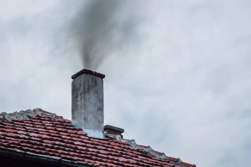 Dym wydobywający się z komina na tle pochmurnego nieba.