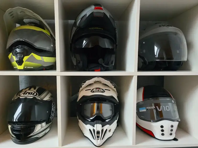 Sześć kasków motocyklowych w różnych kolorach i stylach, ułożonych w sześciu przegrodach.