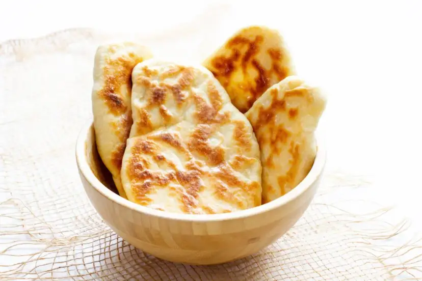 Kilka świeżo upieczonych chlebków naan w drewnianej misce.