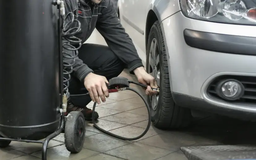 Un homme gonfle un pneu de voiture avec un manomètre et un compresseur.