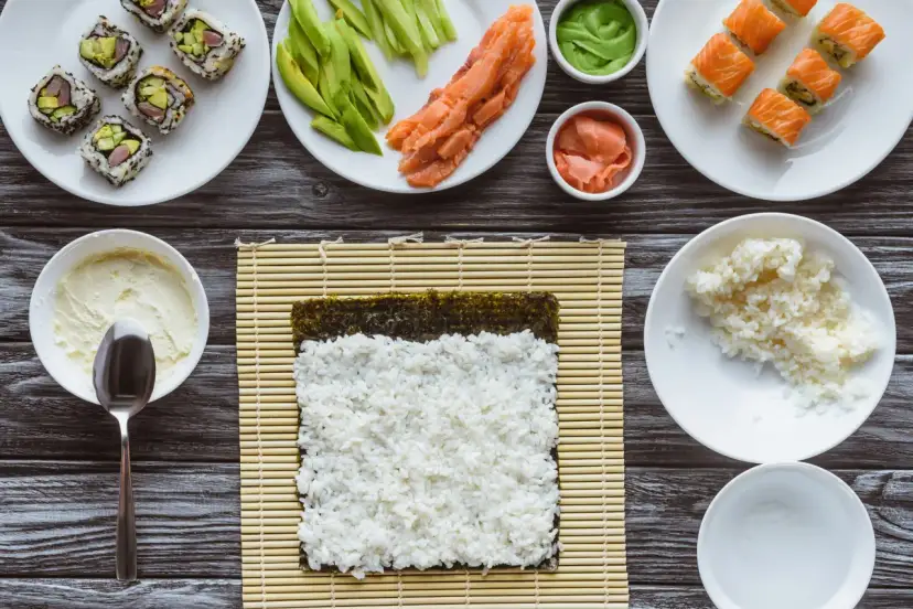 Przygotowanie sushi: ryż, nori, łosoś, awokado, wasabi i marynowany imbir na drewnianym blacie.