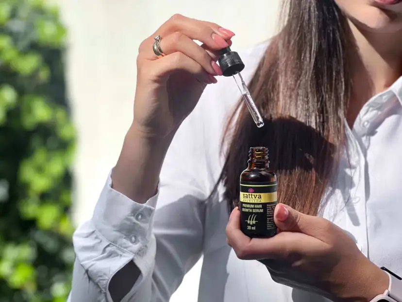 Kobieta trzyma buteleczkę z olejkiem Sattva i pipetkę z serum do włosów.
