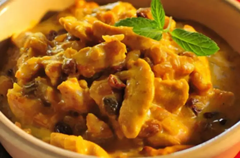 Pyszny kurczak w sosie curry z rodzynkami, ozdobiony listkiem mięty. Idealny przykład, jak zrobić sos curry do kurczaka.