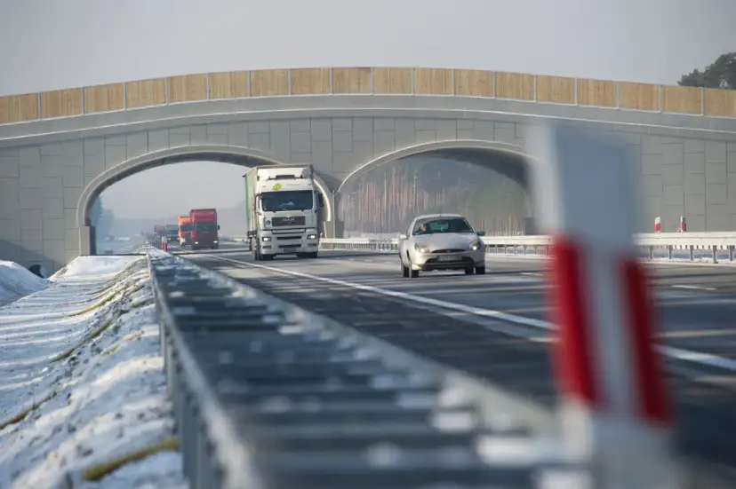 Autostrada A2 z mostem nad jezdnią, jadące samochody i ciężarówki w zimowej scenerii.