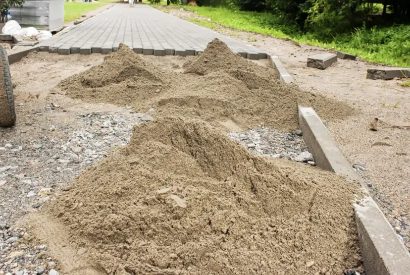 Kopa piasku czeka na ułożenie kostki brukowej. Trudno oszacować, ile piasku na m2 kostki, ale widać, że materiału jest sporo.