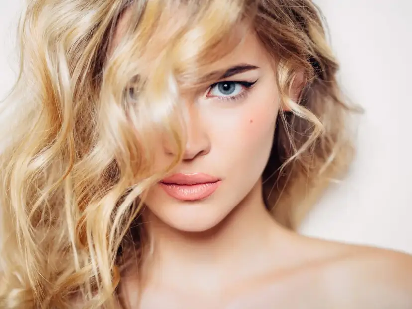 Mujer rubia con ondas, delineado de ojos y labios rosados. Un ejemplo de trucos de belleza para realzar la mirada.