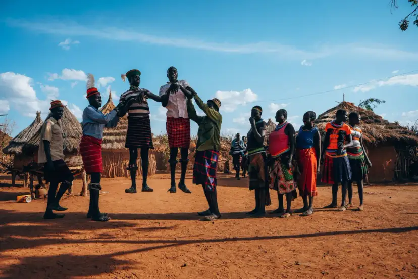 Ludzie w tradycyjnych strojach tańczą przed chatami. Czy Uganda jest bezpiecznie? Tak, w takich miejscach można poczuć się bezpiecznie.