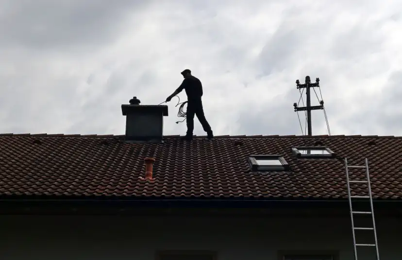 Kominiarz na dachu sprawdza komin. Zastanawiasz się, ile kosztuje przegląd kominiarski?