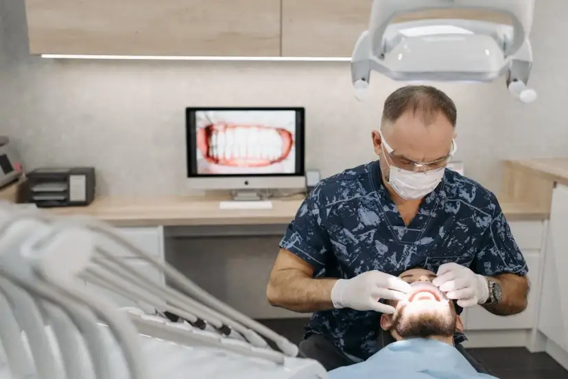 Dentysta w masce i rękawiczkach bada usta pacjenta.