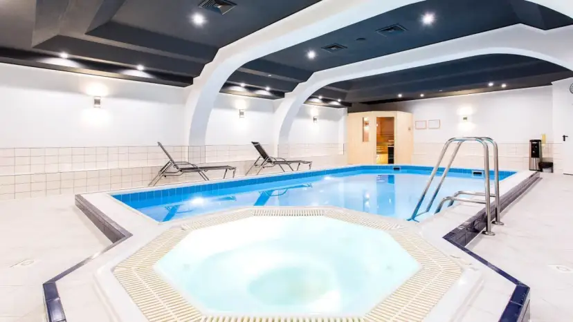 Wnętrze hotelowe z basenem, jacuzzi, sauną i leżakami.