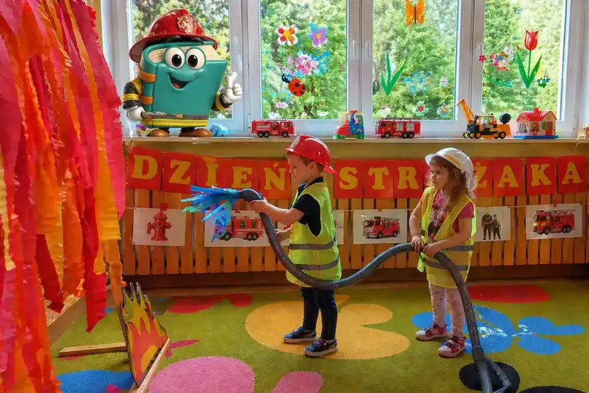 Dzieci gaszą pożar, świetne pomysły na dni otwarte w przedszkolu! Maskotka-książka w stroju strażaka zachęca do zabawy.