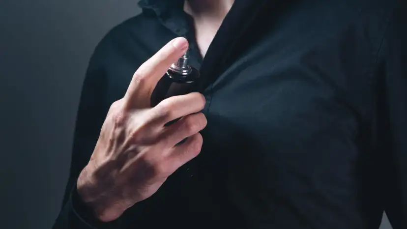 Mann sprüht sich Parfum auf die Brust.