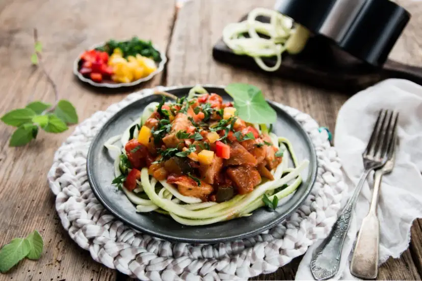 Spaghetti z cukinii z kurczakiem i warzywami w sosie na talerzu.