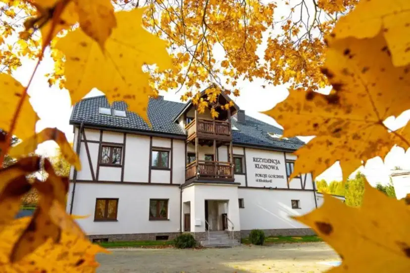 Dom z drewnianymi elementami i balkonem, otoczony jesiennymi liśćmi.