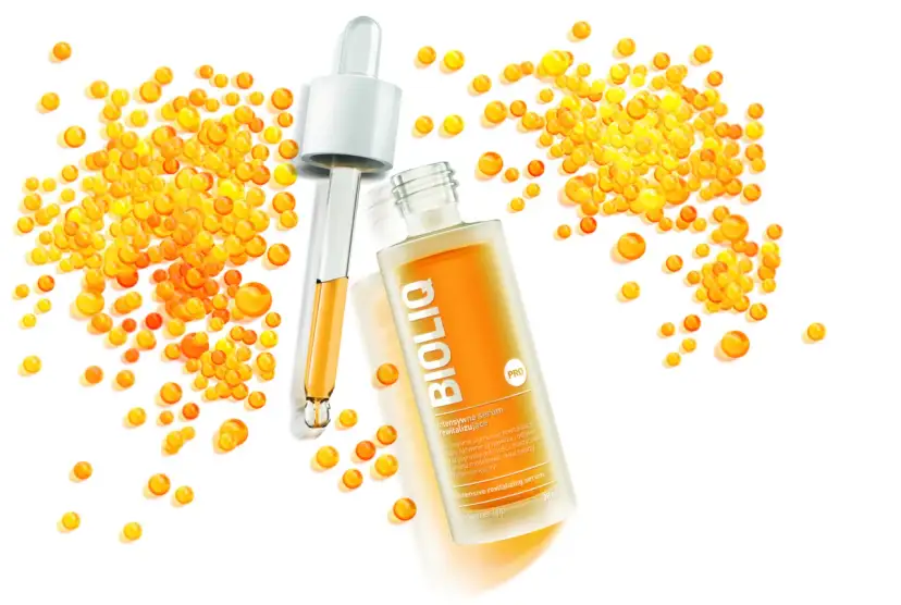 BiolIQ intensywne serum rewitalizujące w buteleczce z pipetą, otoczone kropelkami o pomarańczowym odcieniu.
