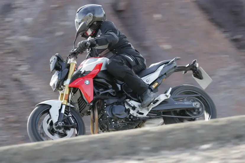 Motocyklista w kasku i kombinezonie pędzi na motocyklu BMW F900R po kamienistym terenie.