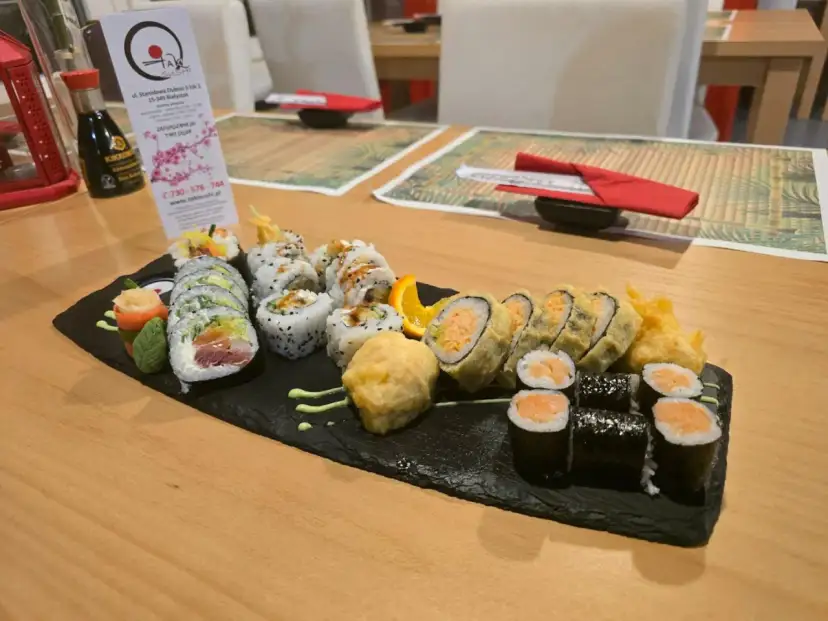 Talerz sushi z różnymi rolkami, w tym smażonymi i z łososiem, na czarnej desce.