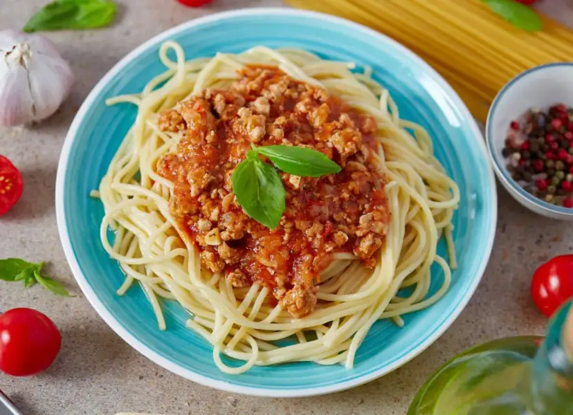Pyszne spaghetti z sosem bolońskim, idealne, gdy zastanawiasz się, jak zrobić sos do spaghetti. Podane na niebieskim talerzu, z bazylią i pomidorkami.