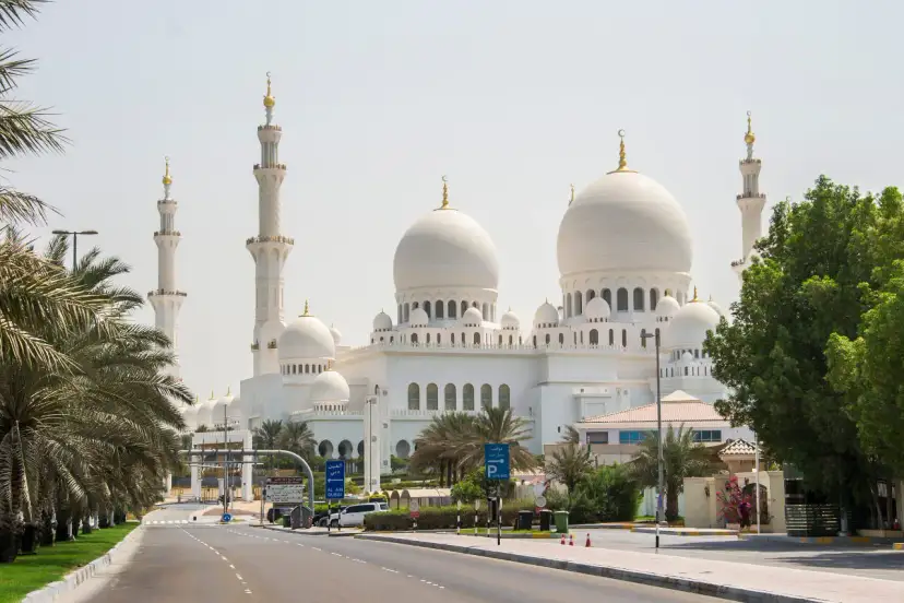 Wielki Meczet Szejka Zajida w Abu Zabi z minaretami i kopułami, otoczony palmami.