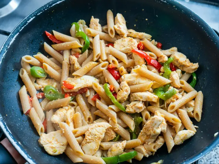 Makaron penne z kurczakiem i papryką w czarnej patelni.