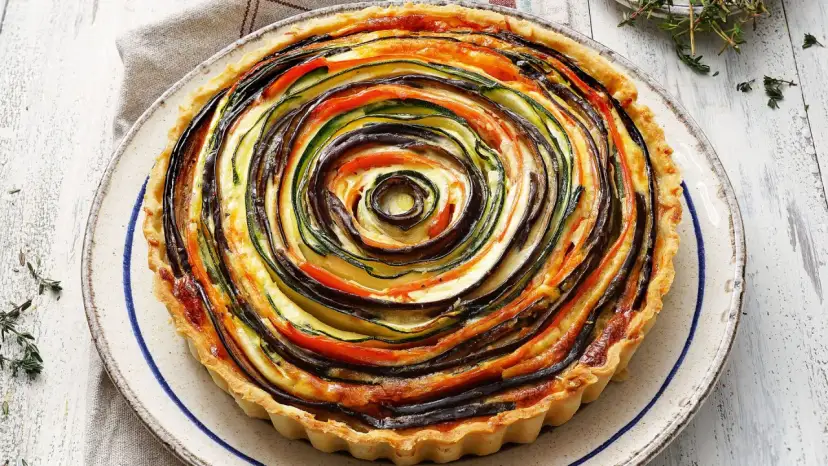 Quiche de verduras con hojaldre, un remolino de calabacín, berenjena y tomate sobre una base dorada.
