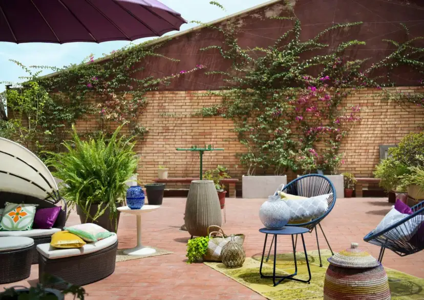 Acogedor **diseño terraza exterior** con muebles de ratán, sillas azules, plantas exuberantes y detalles decorativos en ladrillo.