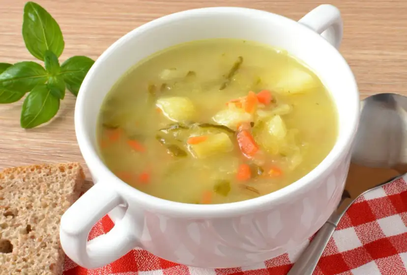 Zupa ogórkowa Ani gotuje się w białej misce, obok kromki chleba i gałązki bazylii.