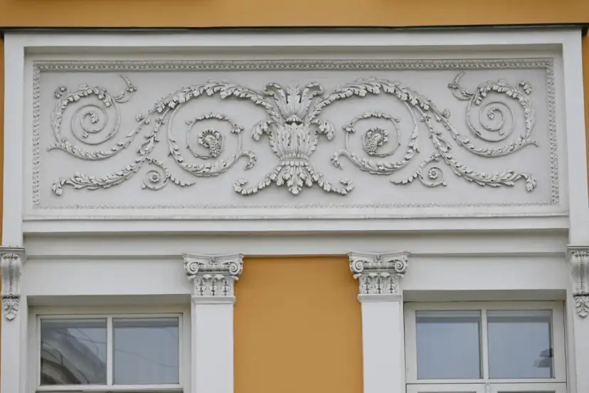 Eleganckie sztukaterie nad oknami to inspiracja, jak ozdobić ścianę zewnętrzną. Wzory liści i winogron dodają klasy.