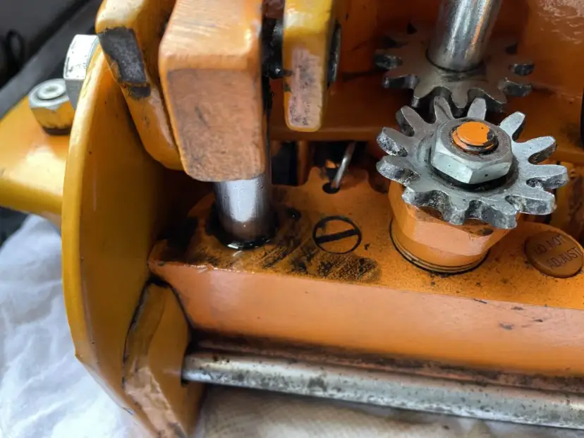Zbliżenie na mechanizm zębatkowy pomarańczowego lewarka z widocznymi śladami oleju.