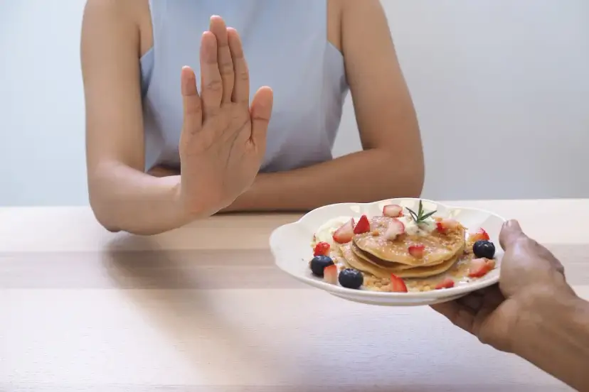 Dłoń odrzuca talerz z naleśnikami i owocami. To symboliczne przedstawienie, jak dieta 1200 kcal efekty po 2 tygodniach motywuje do zdrowych wyborów.