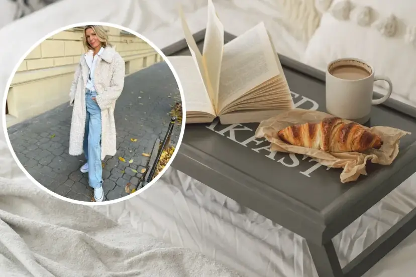 Kobieta w płaszczu z owczej wełny, symbolizującym quiet luxury, cieszy się śniadaniem w łóżku: książka, croissant i kawa.