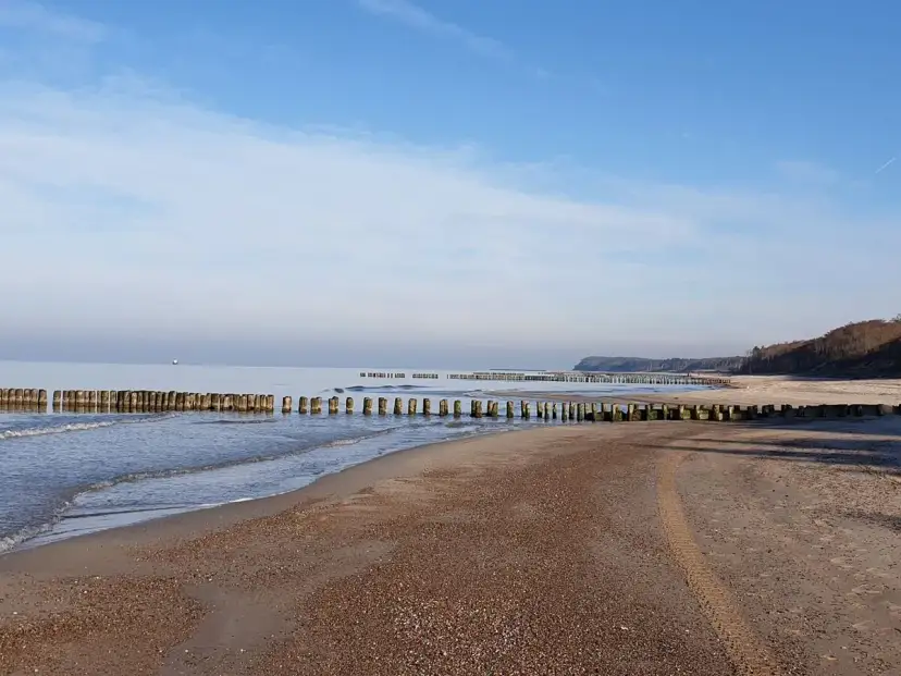 Spokojne morze i pusta plaża w Rusinowie nad morzem. Drewniane falochrony wcinają się w wodę, tworząc malowniczy krajobraz.