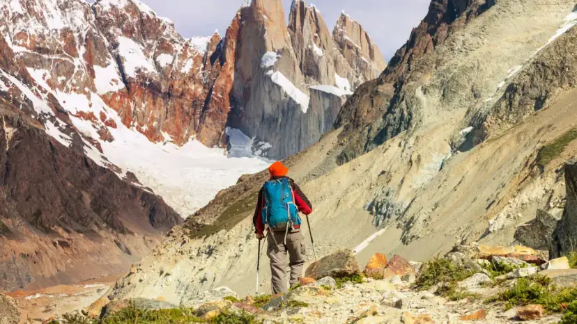 Turysta z plecakiem i kijkami trekkingowymi na tle ośnieżonych gór Patagonii.