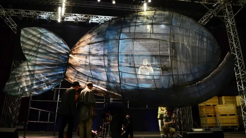 Scena teatralna z wielką, szklaną rybą, w której siedzi człowiek. To może być cud Jonasza.