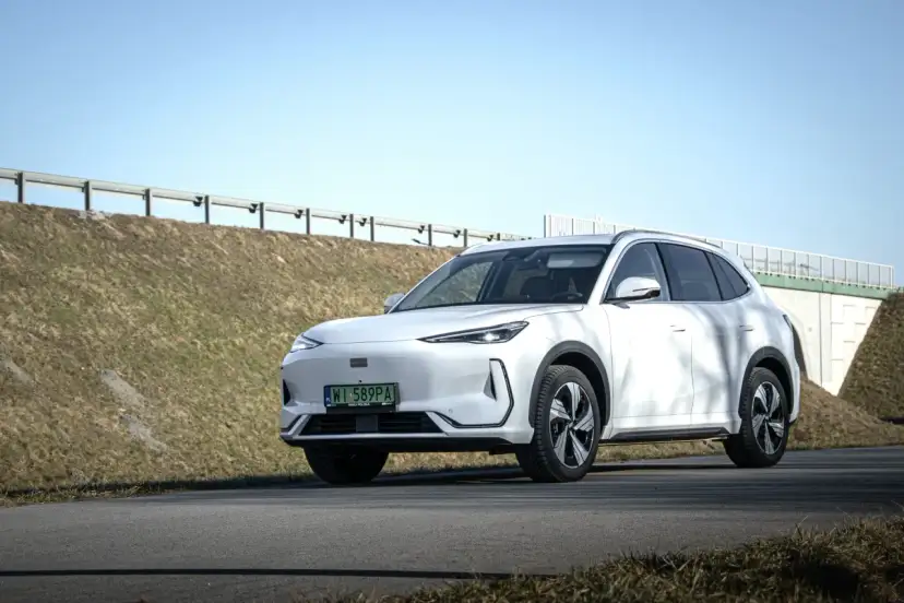 Biały Geely EX5 na tle nieba i nasypu drogowego. Elegancki SUV gotowy na podróż.
