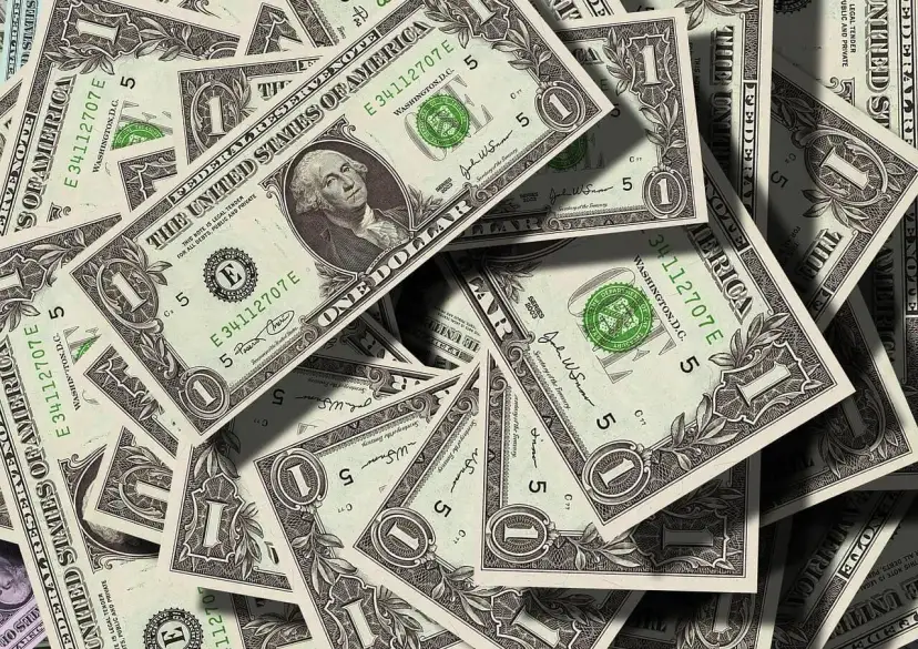 Stosy dolarowych banknotów. Kto ponosi koszty działu spadku u notariusza? Pieniądze mogą pomóc w tej kwestii.