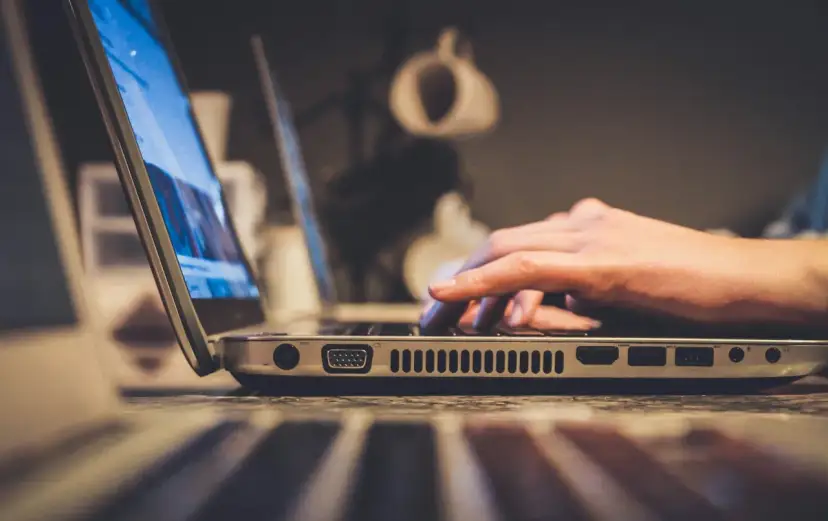 Dłoń pisząca na klawiaturze laptopa, widok z boku.