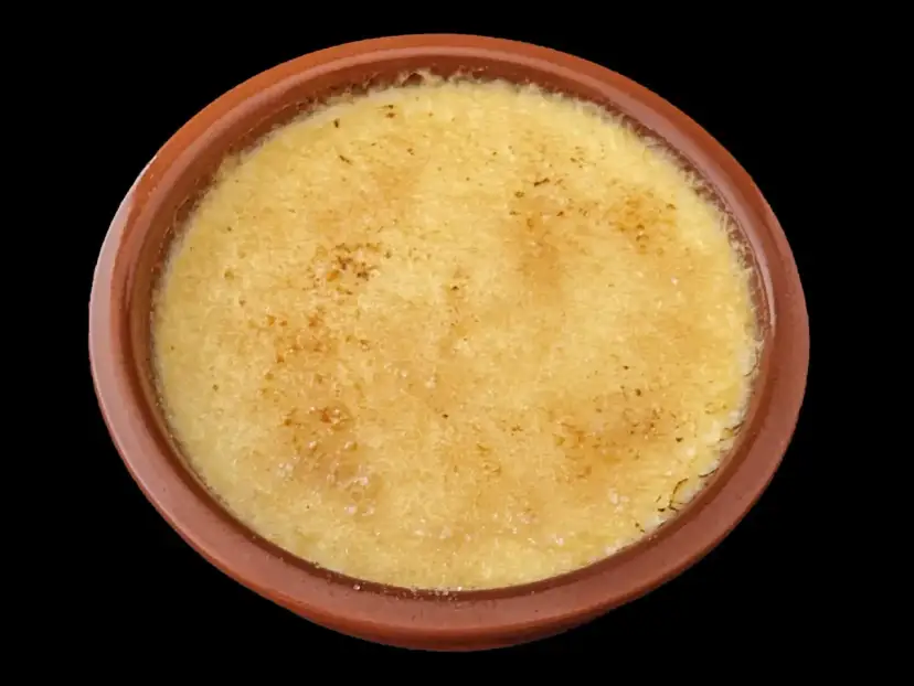 Crème brûlée dans un ramequin en terre cuite, sa surface caramélisée craque sous la cuillère.