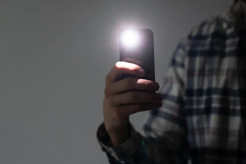 Dłoń trzyma smartfon z włączoną latarką.