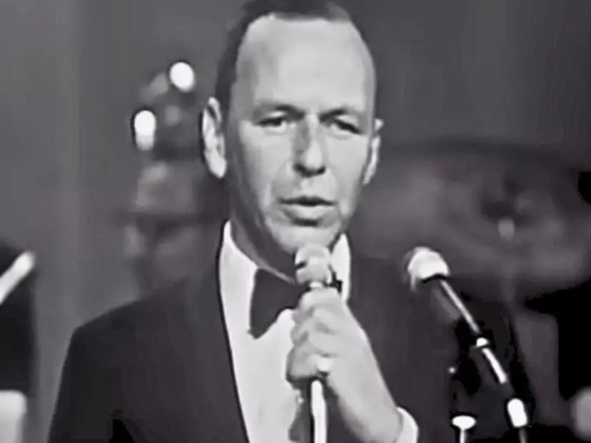 Frank Sinatra śpiewa "Fly Me to the Moon lyrics", ubrany w smoking.