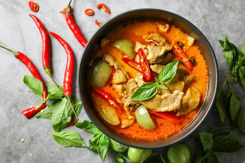 Miseczka czerwonego curry z mięsem, warzywami, papryczkami chili i bazylią.
