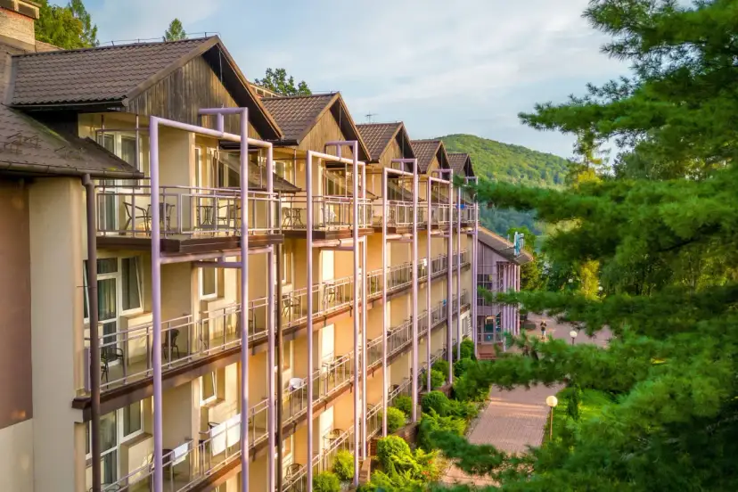 Hotel z balkonami w otoczeniu zieleni i gór.