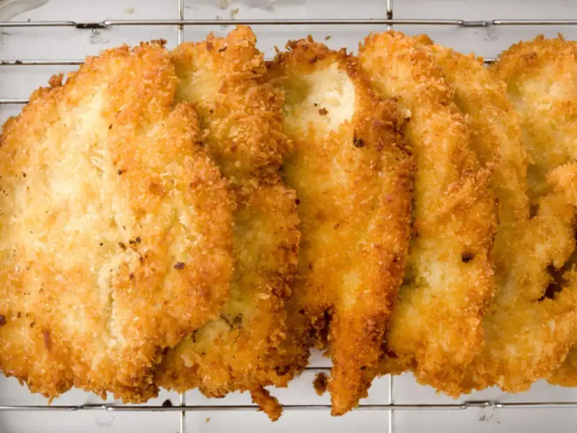 Fileteadas pechugas de pollo empanadas, doradas y crujientes, reposan sobre una rejilla metálica.
